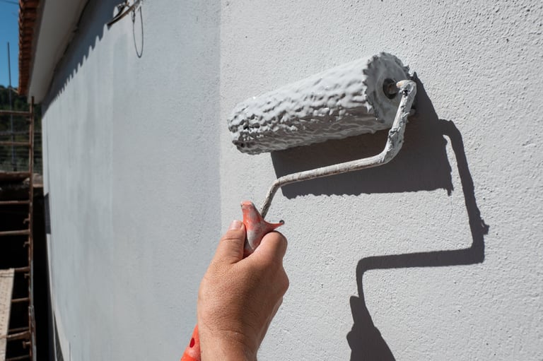 Painter's hand holding a roller filled with paint to paint an exterior wall