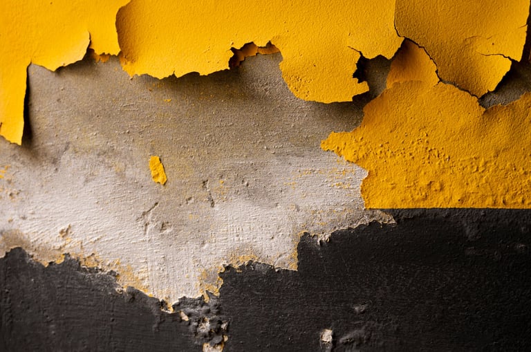 Close-up of a weathered wall surface with flaking yellow paint revealing underlying layers