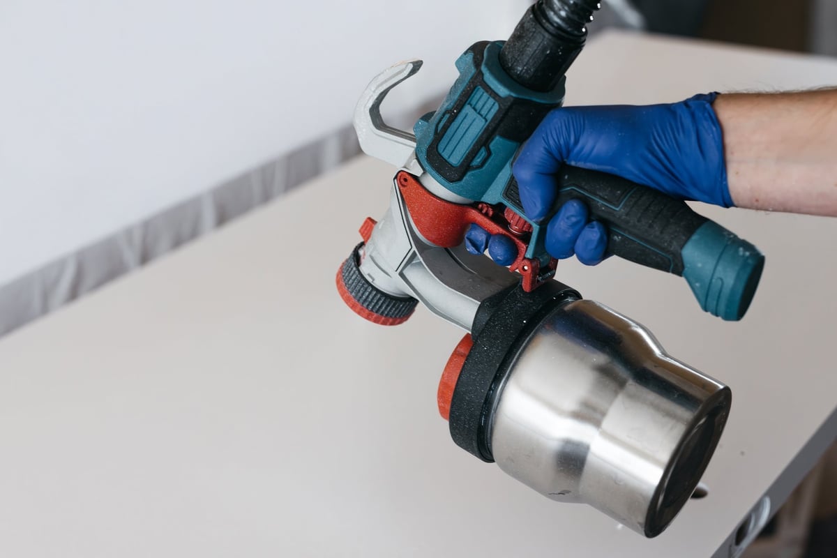 Handheld spray gun with stainless steel cup held by gloved hand ready for coating applications