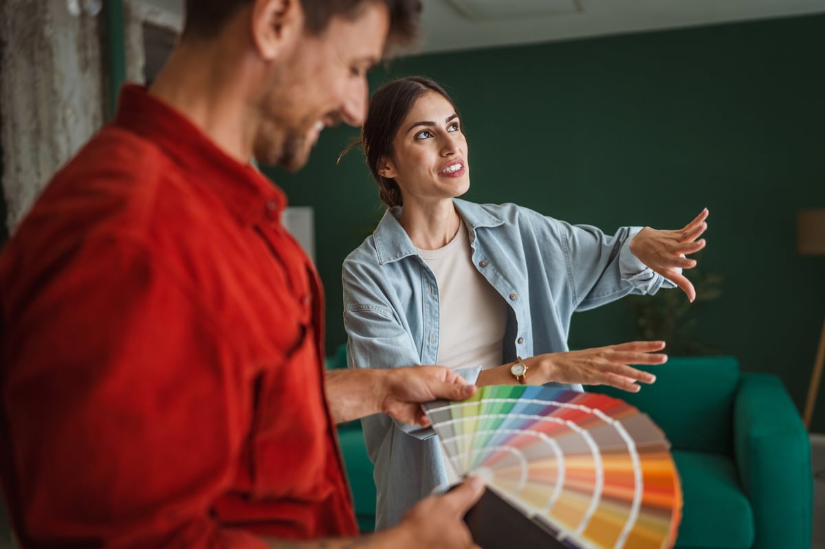 Young couple comparing paint swatches and planning interior colors for a cozy modern living room during a home renovation