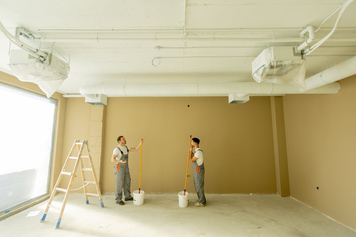 Two painters are focused on painting a wall beige in a well-lit room