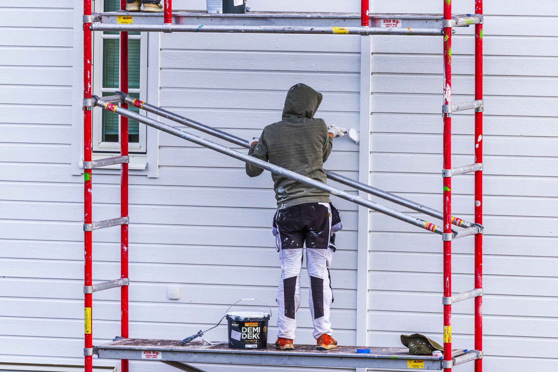 Worker painting the exterior wall of a building from metal scaffolding