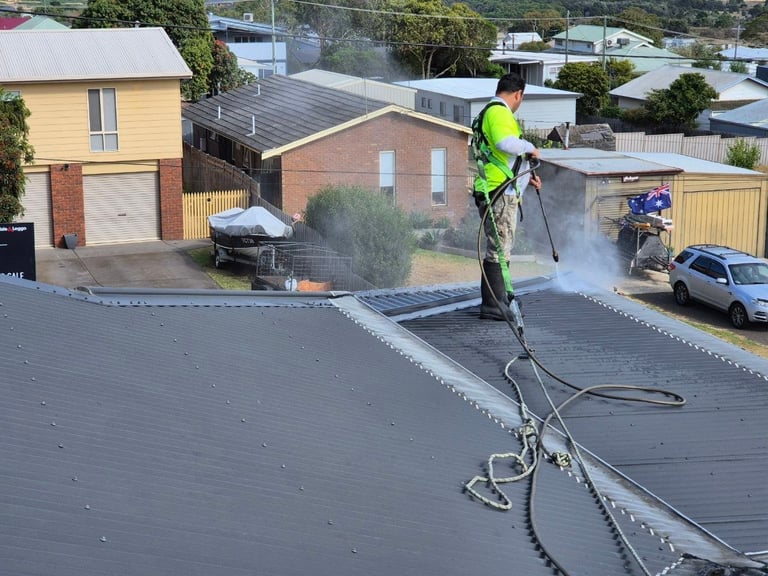 Worker in high-visibility gear applying seal coating to a residential driveway with spray equipment