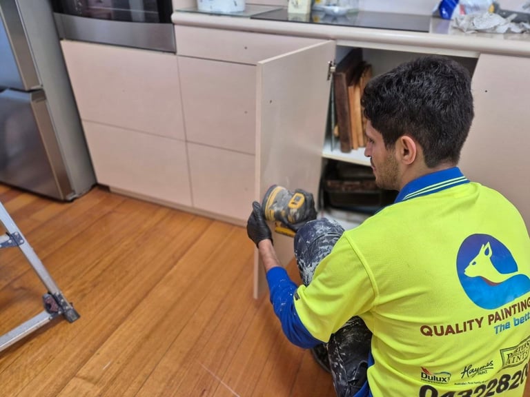 Painter in neon yellow Quality Painting shirt with blue gloves working on white kitchen cabinets