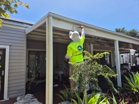 Construction worker in high-visibility vest reaching up on covered patio of residential home with plants