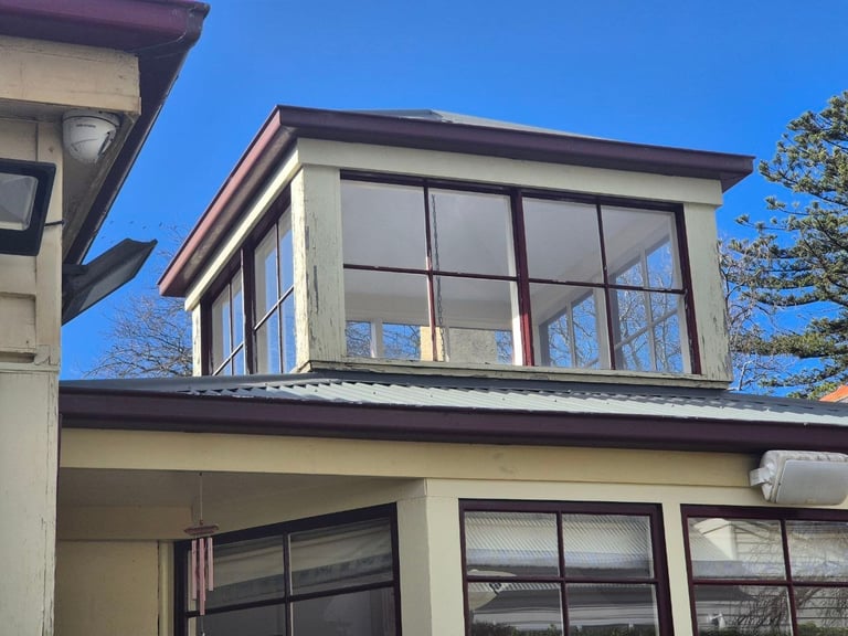 Modern two-story home with large windows, tan exterior, and dark trim against clear blue sky