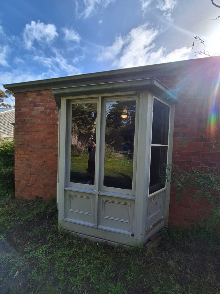 White-framed sunroom or conservatory extension attached to red brick house with garden in background