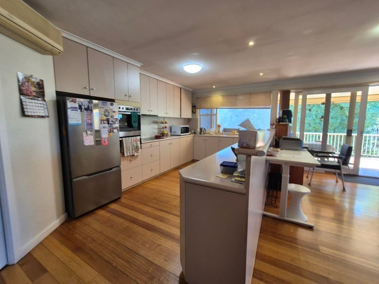Modern kitchen with white cabinetry, stainless steel appliances, brown island, wood flooring, and sliding glass doors opening to a deck view