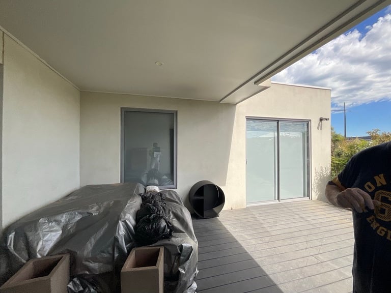 Modern home terrace with gray composite decking, white walls, glass doors, and boxes with plastic bags stacked on the floor