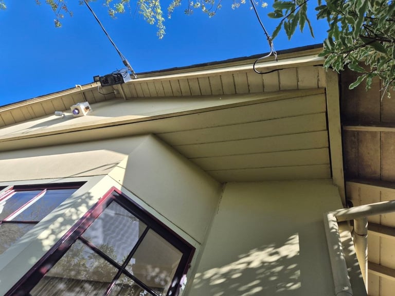 Beige residential house exterior with covered porch, open soffit, and clear blue sky overhead.