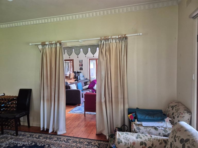 Beige curtains hung on a rod dividing a living room with cream walls and hardwood flooring