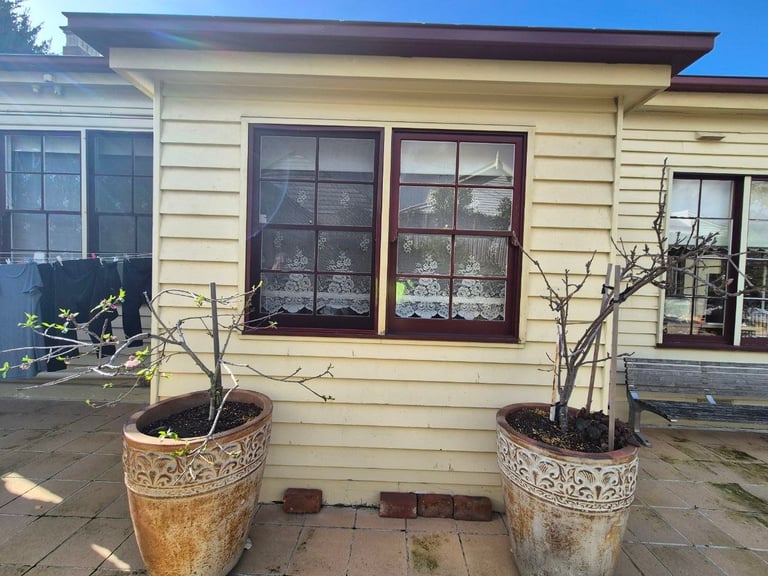 Front of house with cream-colored siding, double red-trimmed windows, and two decorative planters on either side of brick entrance