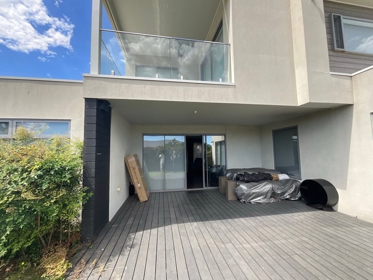 Modern patio area with dark wooden deck, glass sliding doors, and construction materials stored outside a contemporary house