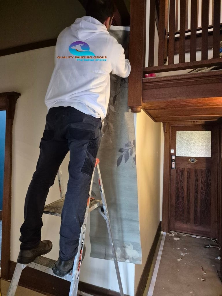 Painter on ladder wearing Quality Painting Group shirt working on interior wall of home