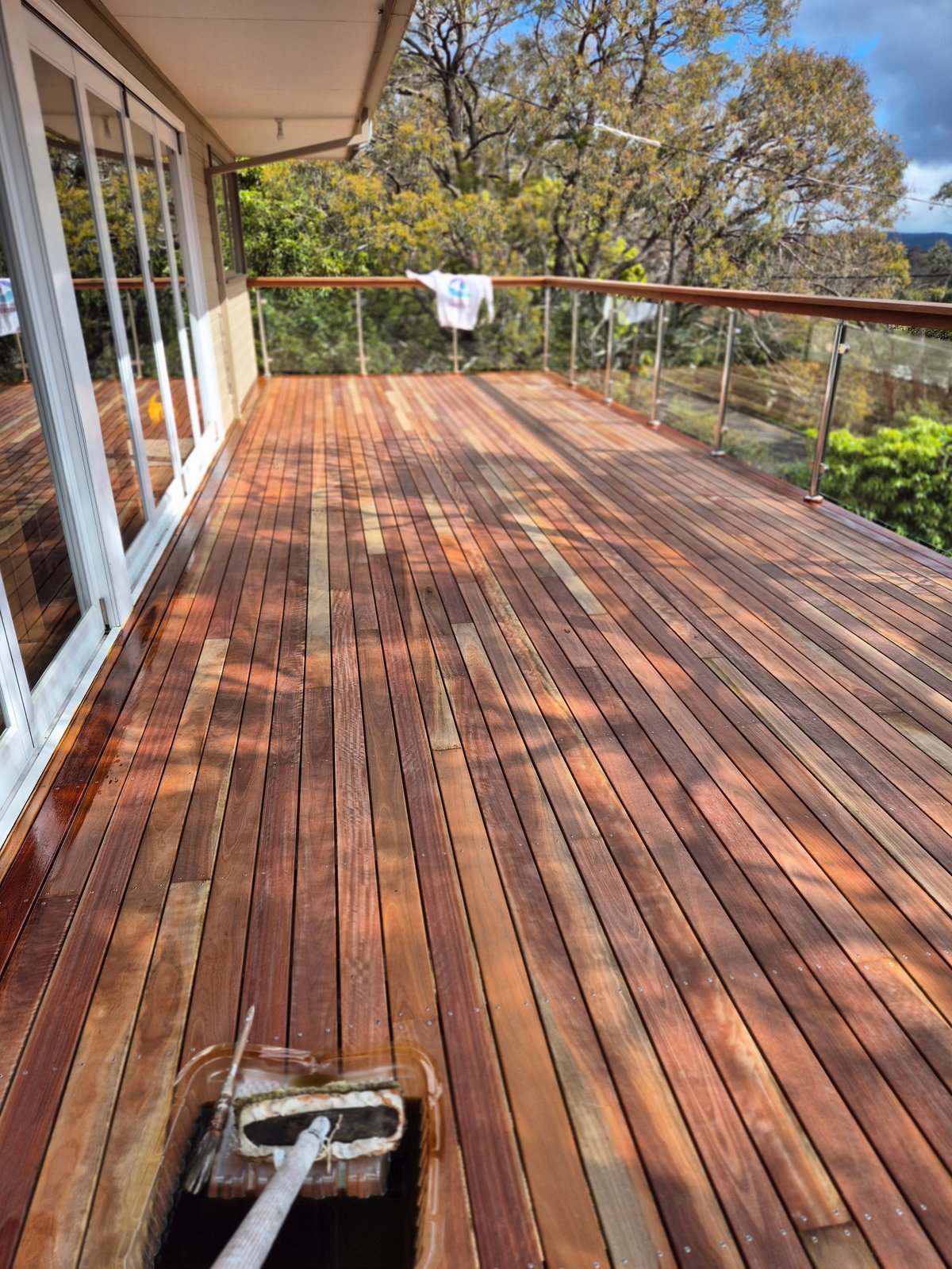 Wooden deck with glass doors and metal railing overlooking forested hillside landscape