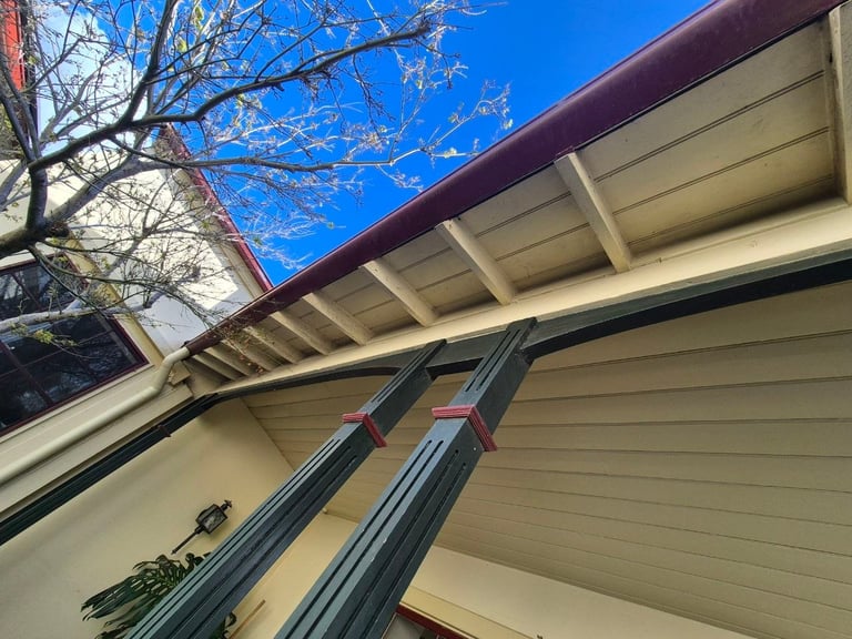 Modern home roof with cream siding, burgundy trim, and support struts against clear blue sky and bare tree branches
