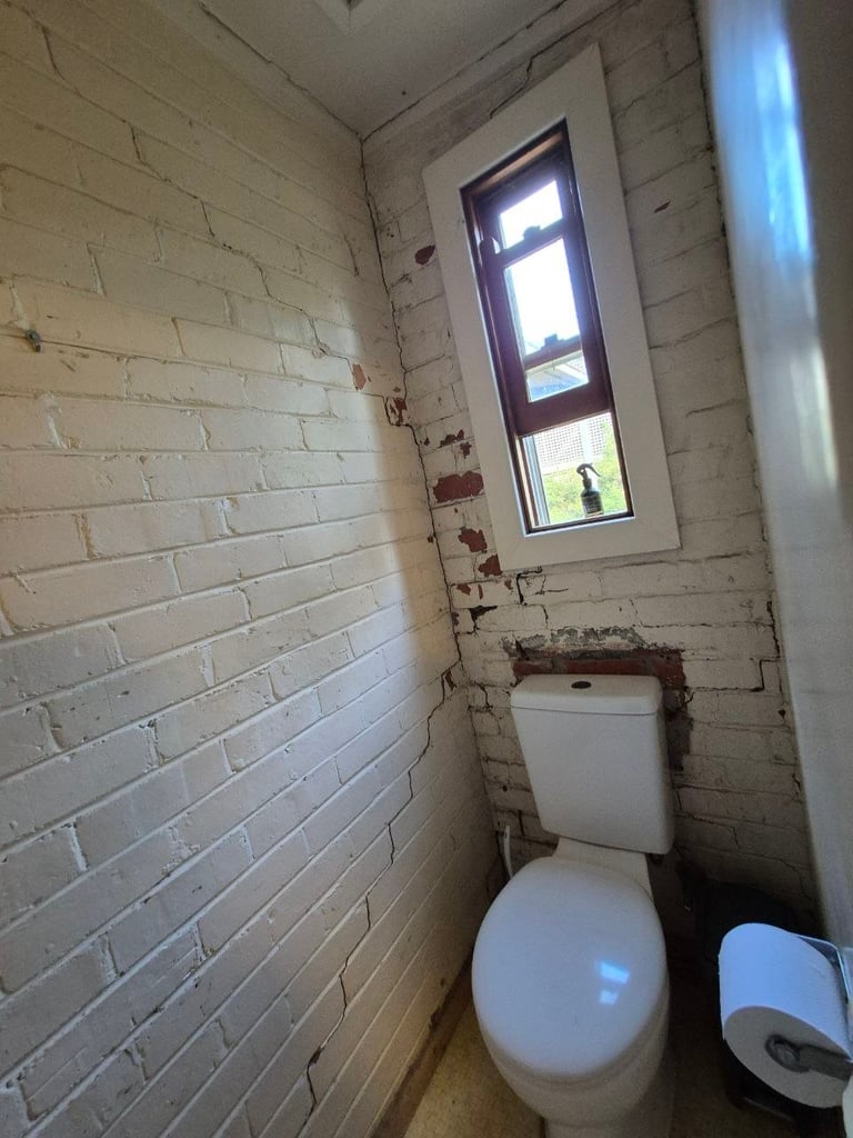 Small bathroom with white brick walls, toilet, window with natural light, and white soap dispenser