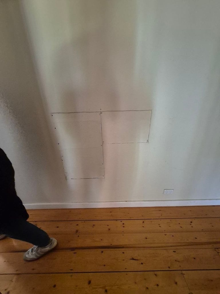Persons foot visible next to rectangular outlines marked on white drywall above wooden floor