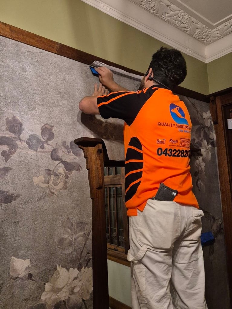 Painter in orange safety vest installing or measuring decorative wall trim in an ornate room with sage green walls