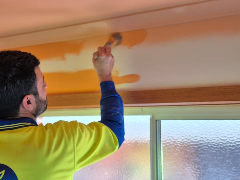 Man in yellow and blue shirt reaching up to inspect or work on a textured orange ceiling
