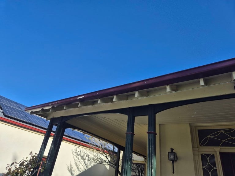 Modern house exterior with cream-colored walls, dark-framed pergola overhang, and clear blue sky above