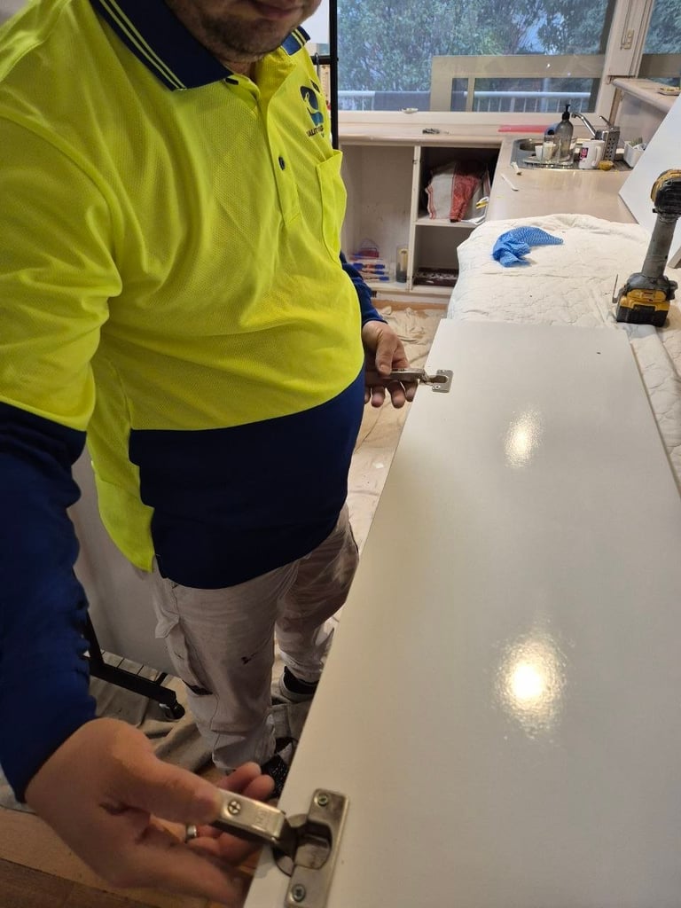 Worker in yellow safety jacket installing or repairing a white countertop or cabinet in a kitchen workspace