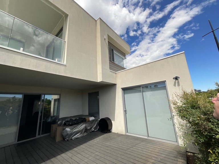 Modern two-story white house with deck, large windows, and blue sky with clouds