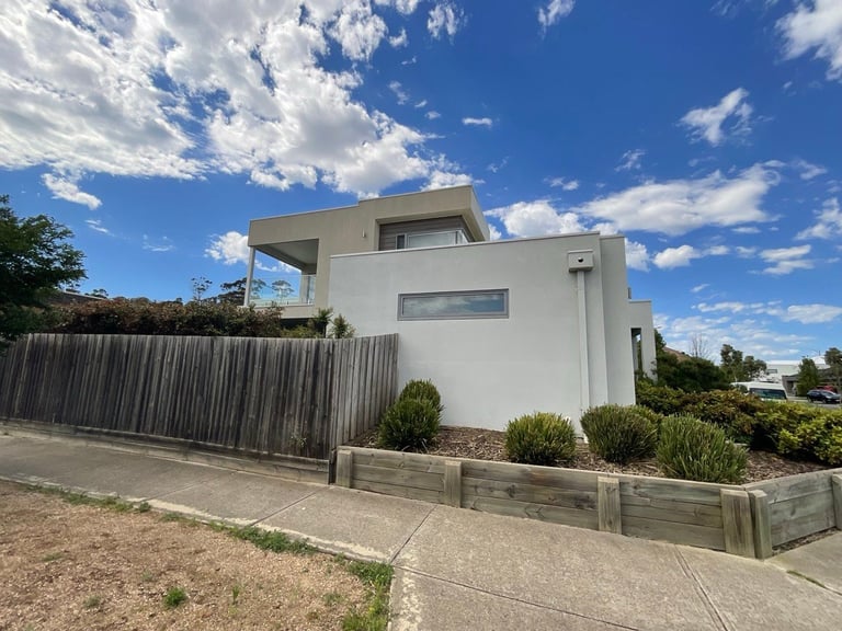 Modern white cubic house with wooden fence and landscaping under blue sky with clouds